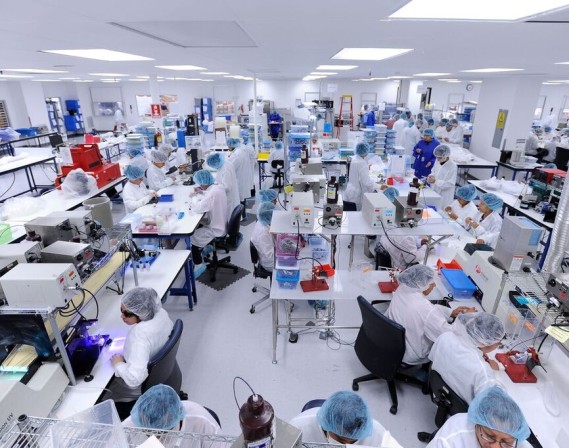 Medical device assembly laboratory with many technicians in white lab coats with blue hair nets.